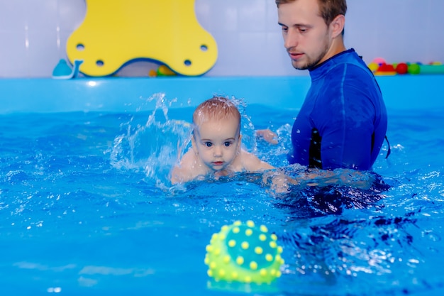 Coach teaches the baby to swim in the pool