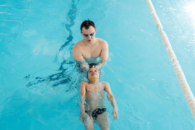 A coach teaches a sevenyearold boy to swim in a modern swimming pool Learn to swim Development of childrens sports Healthy parenting and promotion of childrens sports