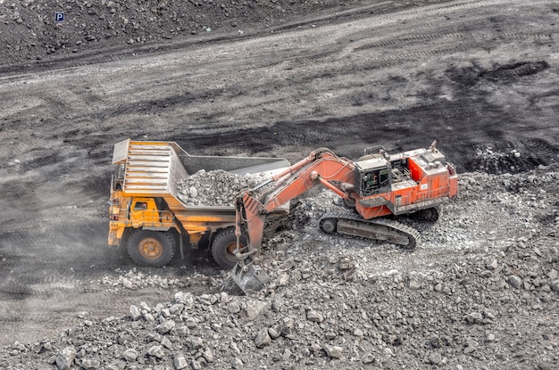 Coal mining in a quarry. A hydraulic excavator loads a dump truck. Loading of coal into the body of a truck.