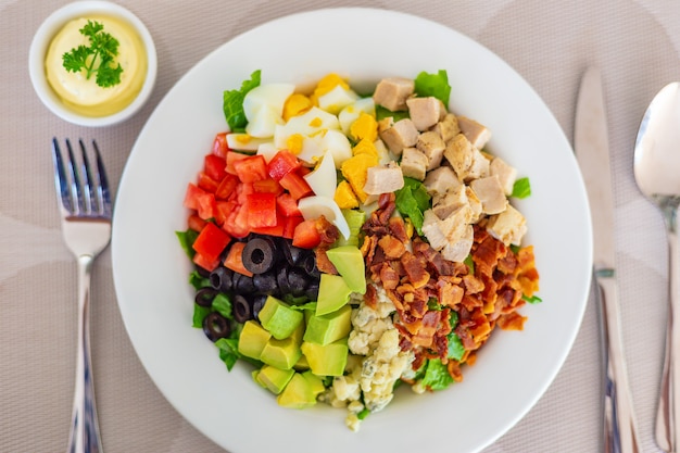 Cobb salad on white plate, with bacon, blue cheese, grilled chicken, cubed cut tomatoes and avocados