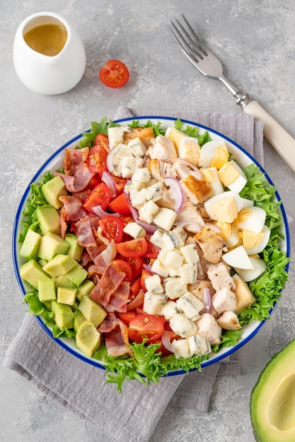 Cobb salad with fried chicken avocado fresh tomatoes egg bacon and cheese on a plate selective focus