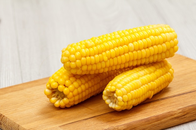 Cobs of cooked corn on cutting board with wooden background.