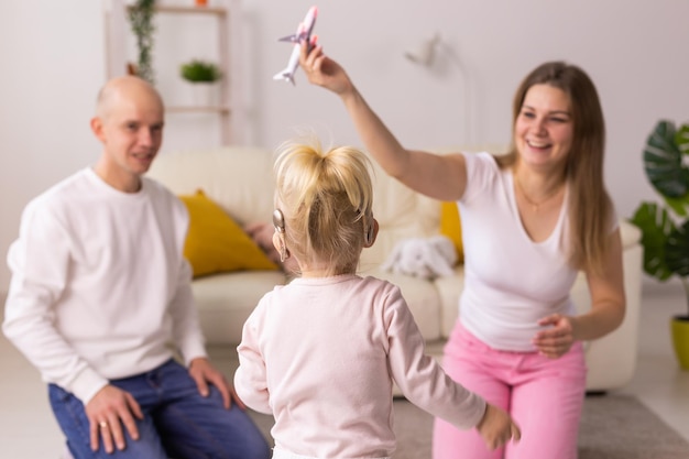 子供の女の子の頭に人工内耳を装着し、母親と父親の補聴器と難聴で遊んでいます