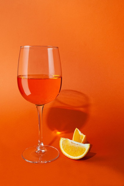 Cocktail aperol spritz in een glazen beker naast het glas zijn twee plakjes sinaasappel op een effen oranje achtergrond hard licht scherpe schaduwen close-up plaats voor tekst