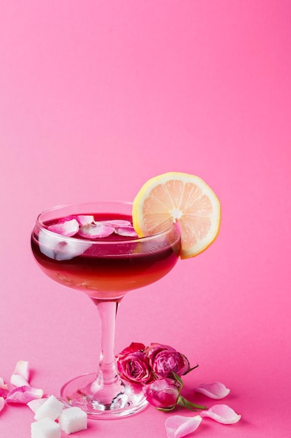 Cocktail bar background. Rose beverage with vodka, pineapple juice and strawberry champagne served with lemon slice and rose petals at pink backdrop, copy space