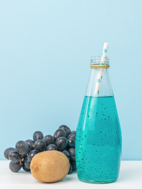 Коктейльная бутылка с семенами базилика с коктейльной трубкой на синей поверхности