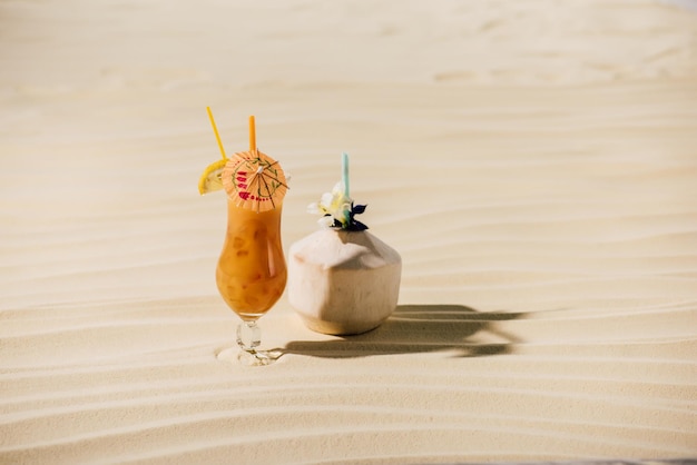 Cocktail in coconut with flower and cocktail in glass on sandy beach