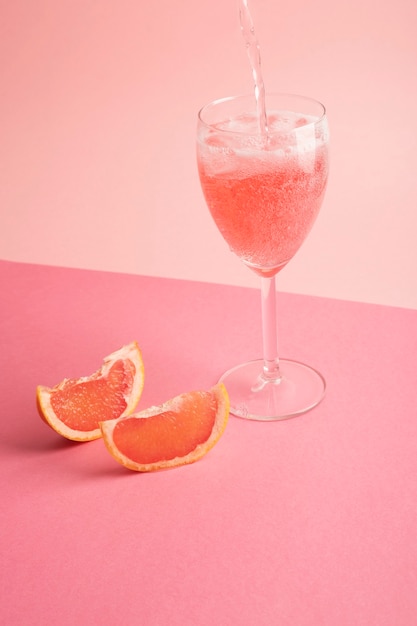 cocktail falling into the glass on a pink surface with grapefruit around