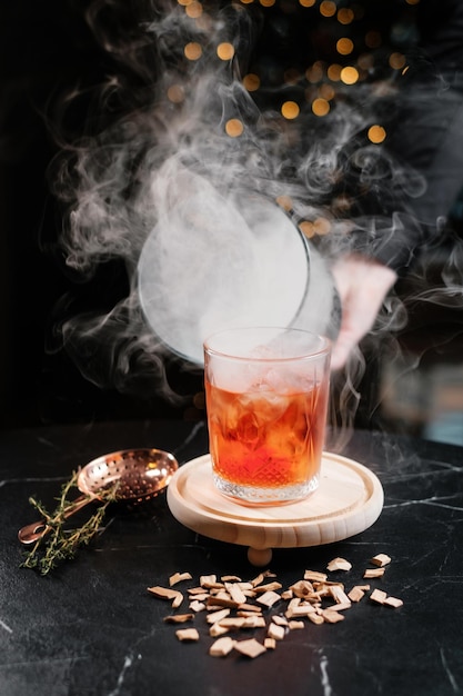 Cocktail geserveerd op een houten bord met een glazen koepel en rook De barman die de cloche opheft Concept van esthetische drankjes serveren