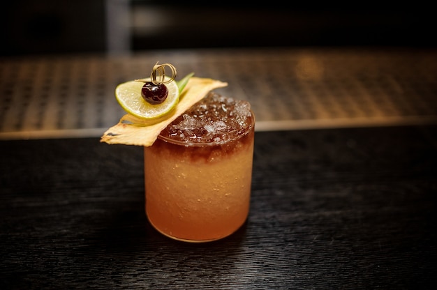 Bicchiere da cocktail riempito con gustosa bevanda alcolica dolce con ghiaccio e fette di frutta sul bancone del bar