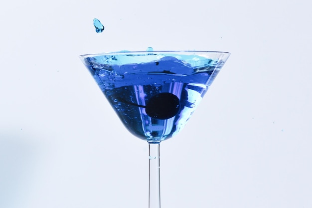 Cocktail met blauwe vloeistof in glas Glas met blauw water gieten met vloeistof met spatten en druppels Martiniglas vullen met alcohol met spatten op witte achtergrond Verfrissend drankje concept