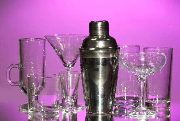 Cocktail shaker and glasses on color background