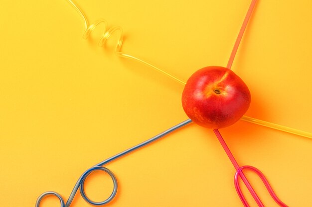 Cocktail straws in peach on yellow background, concept of juicy peach