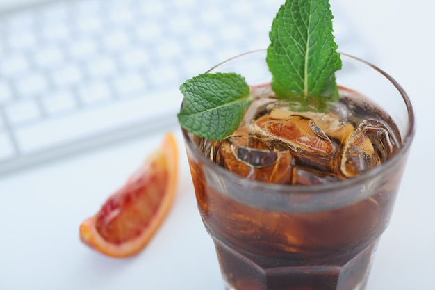 Cocktail whiskey cola with ice in a glass. It stands on the office desk on the keyboard. View from above.