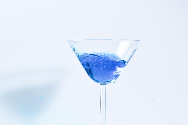 Cocktail with blue liquid in glass Glass with blue water pouring with liquid with splashes and drops Martini glass filling with alcohol with splashes on white background Refreshing drink concept