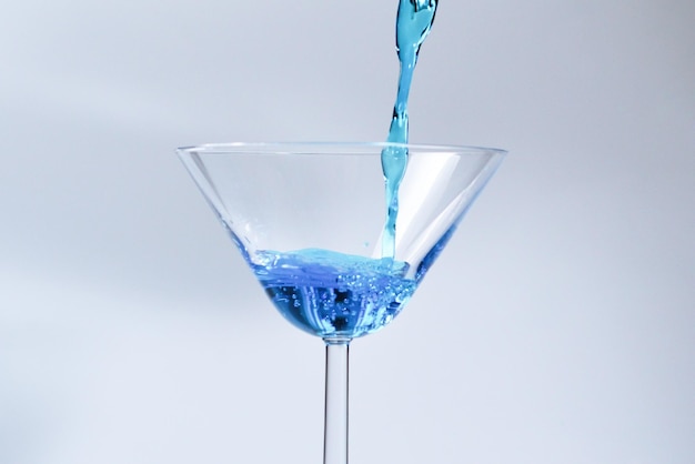 Cocktail with blue liquid in glass Glass with blue water pouring with liquid with splashes and drops Martini glass filling with alcohol with splashes on white background Refreshing drink concept