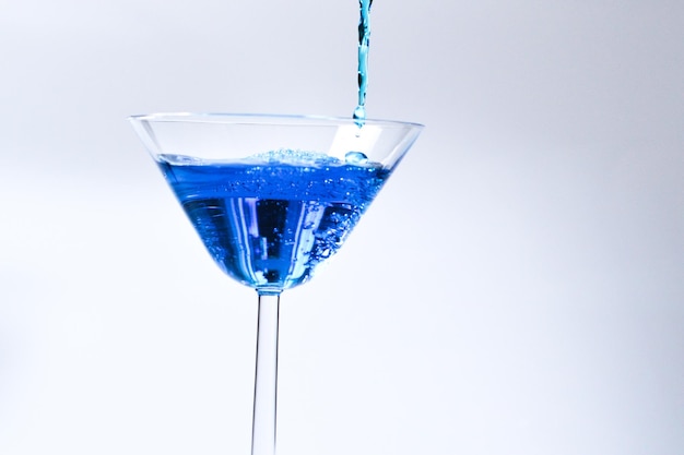 Cocktail with blue liquid in glass glass with blue water\
pouring with liquid with splashes and drops martini glass filling\
with alcohol with splashes on white background refreshing drink\
concept