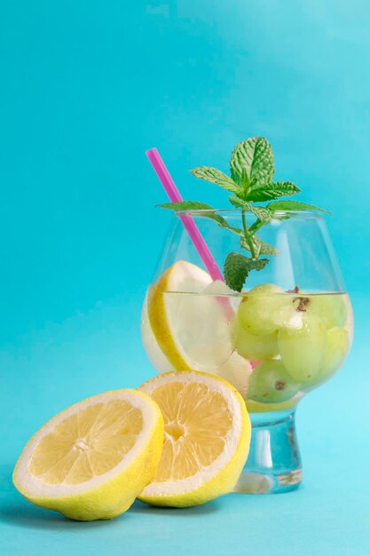 Cocktail with grapes and lemon slices in front of the glass half a lemon all in blue summer drink