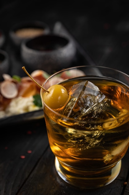 Cocktail with ice and cherry on a dark table Snacks for a cocktail