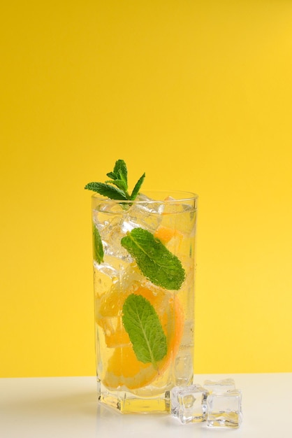 Cocktail with lemon and mint on a yellow background Copy space