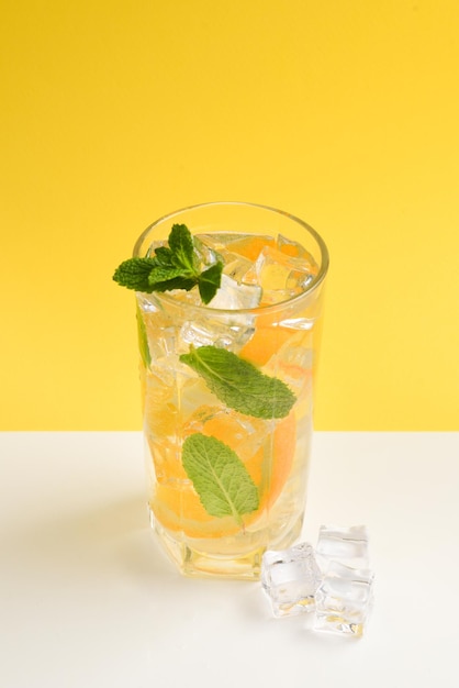 Cocktail with lemon and mint on a yellow background Copy space
