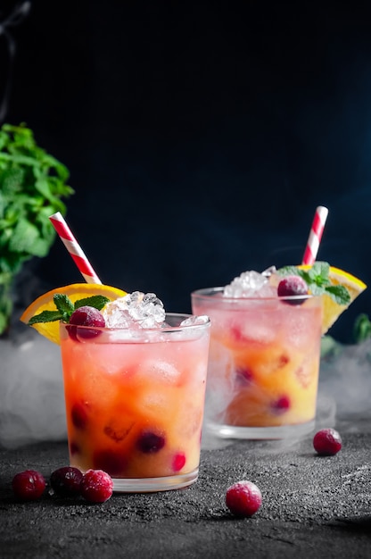 Cocktail with Rum or  Soda, Cranberry, Orange Juice, Lime and Mint in the Glass with Smoke on Dark Grey wall