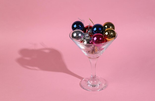 Cocktailglas met kerstballen speelgoed op roze achtergrond Minimaal kerstfeest concept