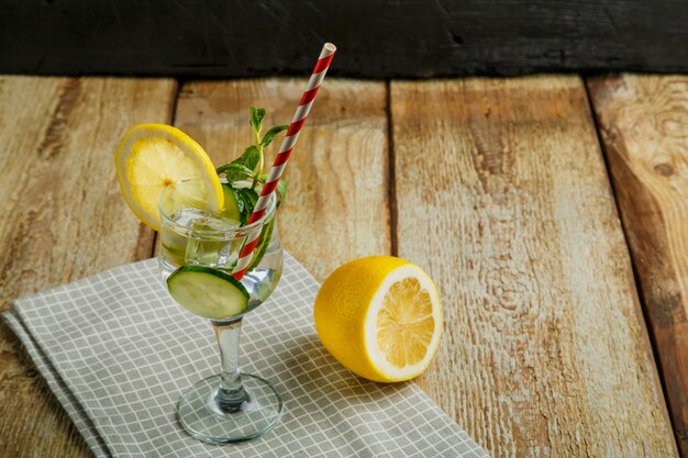 Cocktailkomkommerwater met citroen en munt in een glas op een servet op een zwarte ondergrond in de buurt van citroen en komkommer