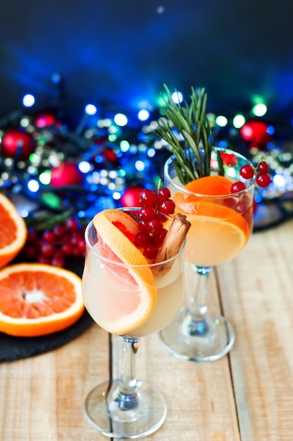 Cocktails with citrus fruits, red currant, cinnamon sticks and green rosemary in wine glasses.