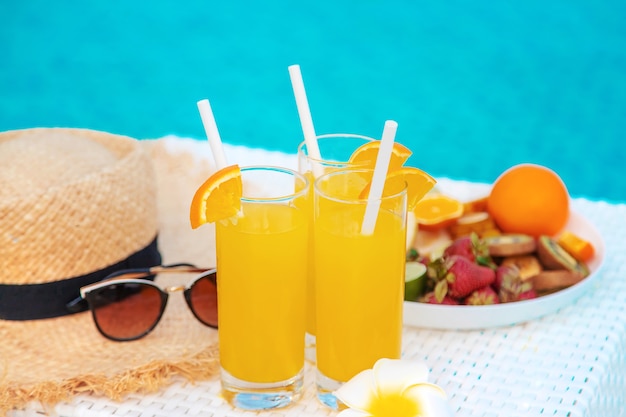 Cocktails, zonnebrillen, strohoed en vers fruit in een witte kom bij het zwembad