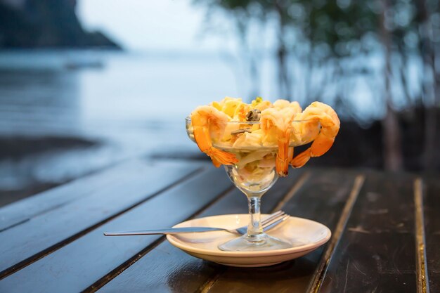 Cocktailsalade met garnalen en zeevruchten op een houten tafel tegen de achtergrond van de zee.