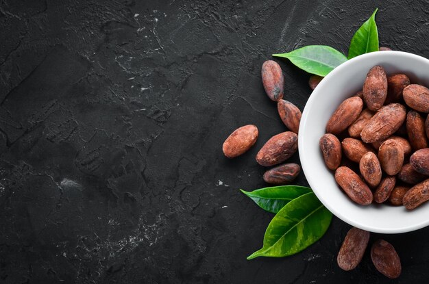 Cocoa beans in a bowl on a black background. Top view. Free copy space.