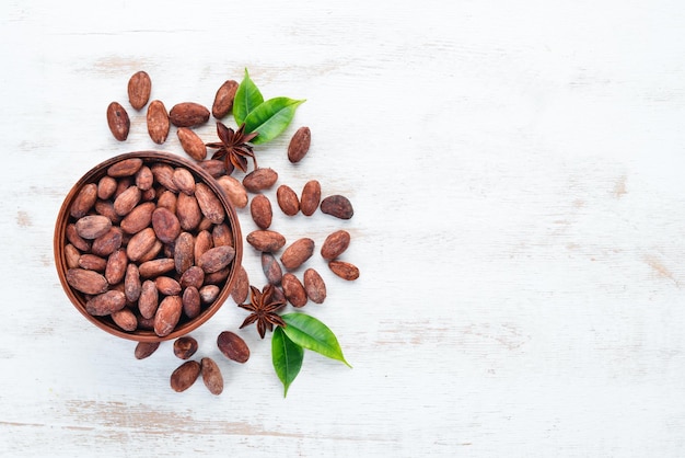 Cocoa beans in a bowl on a white wooden background Top view Free copy space