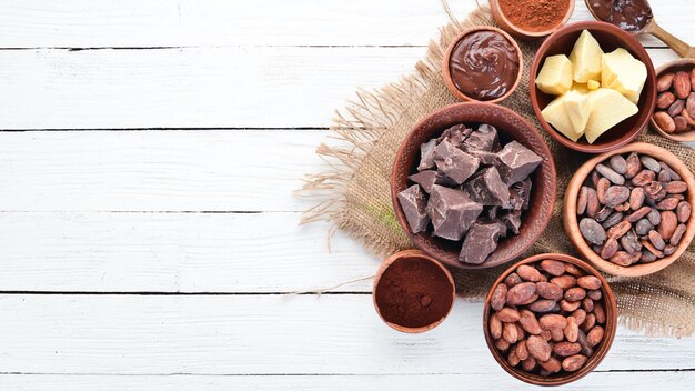 Cocoa beans chocolate cocoa butter and cocoa powder on a white wooden background Top view Free copy space