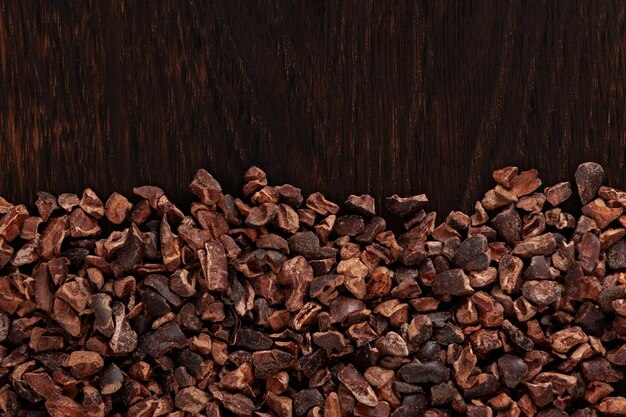 갈색 나무 판자에 있는 코코아 닙 껍질을 벗기고 으깬 코코아 콩의 바삭바삭한 조각