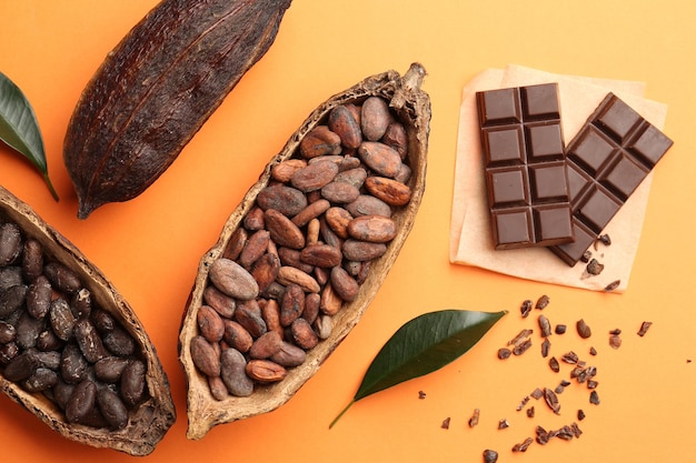 cocoa pods with beans and chocolate on orange background flat lay