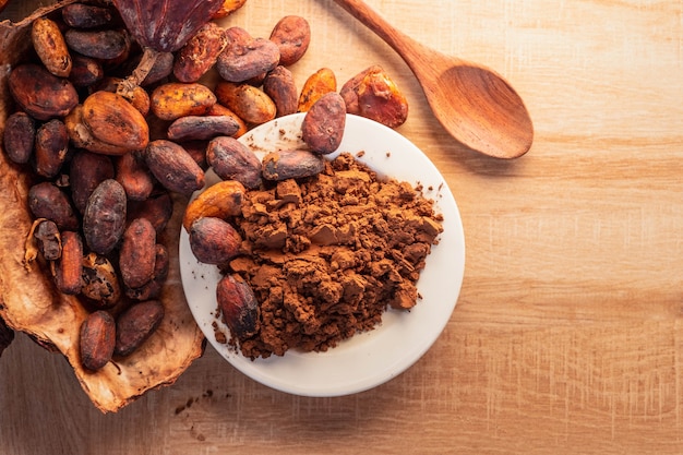 Cacao in polvere e fave di cacao con baccelli di cacao su fondo di legno.