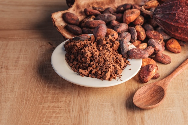 Cocoa powder and cocoa beans with cocoa pods on wooden table.