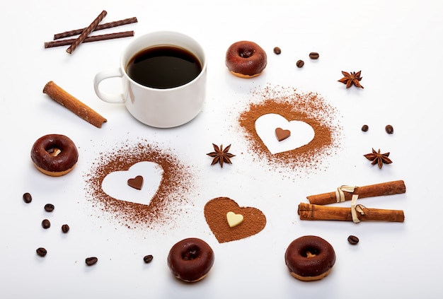 Cocoa powder in the shape of heart, mint sticks and a cup of espresso with chocolate doughnuts.