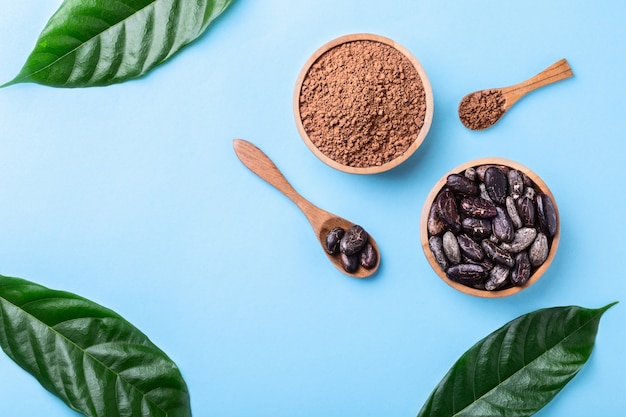 Cocoa powder and whole cocoa beans in wooden bowls with fresh leaves