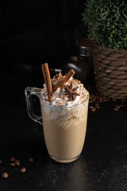 Cocoa with whipped cream, cinnamon sticks and star anise in a transparent mug.