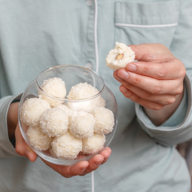 Coconut candy balls in glass bowl in hands of woman