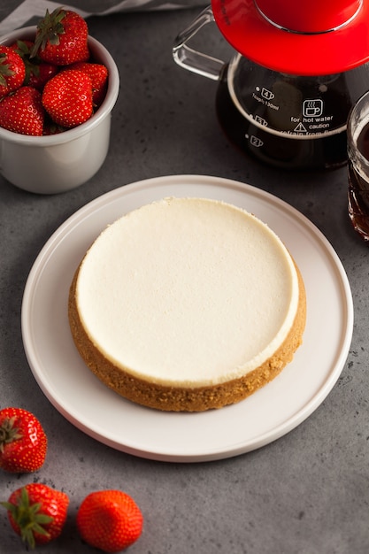 Coconut cheesecake on a round plate. tAeapot with black coffee and a mug of fresh strawberries.