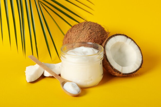 Coconut, cosmetics and palm branch on yellow table, close up