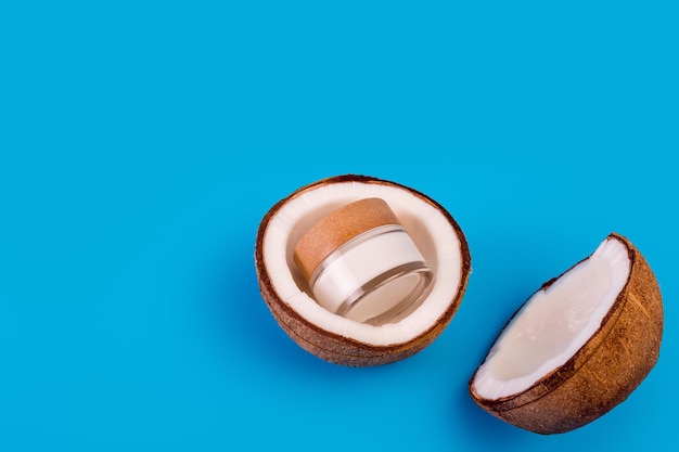 Photo coconut cream in glass jar with fresh coconut split in half on isolated blue background