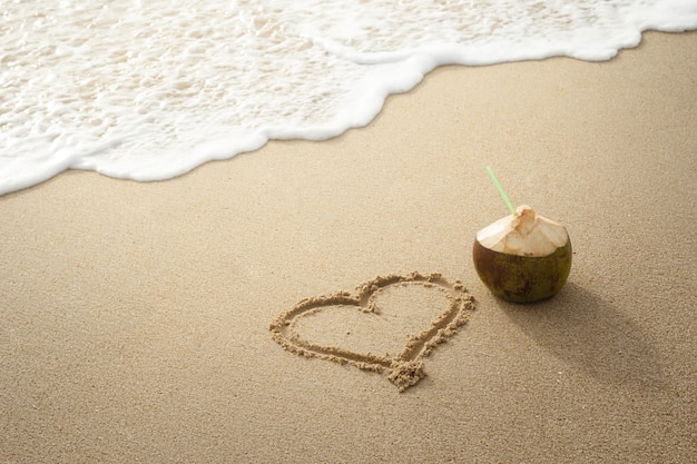 Coconut drink and drawn heart on the sand