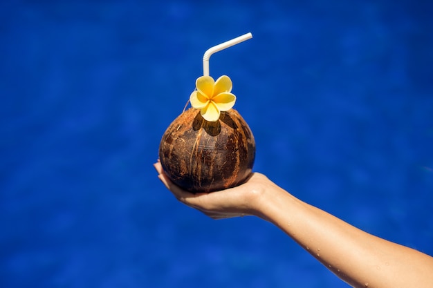 Coconut drink in woman hand on swimpool