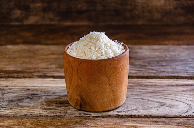 Coconut flakes in a wooden bowl on a wooden background.