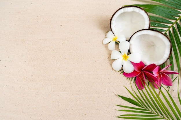 Coconut fruit and frangipani flowers on sand beach background.