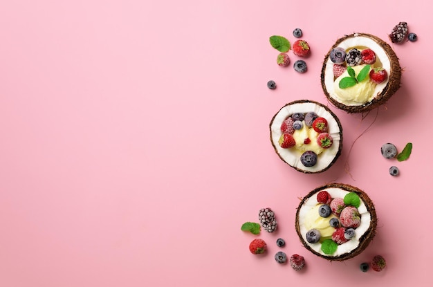 Coconut ice cream with fresh berries in coconuts halves on pink background with copy space Top View Pop art design creative summer concept Food in minimal flat lay style